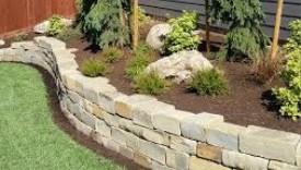 Image of a retaining wall installation project in a yard with green grass and a garden at an upper level.