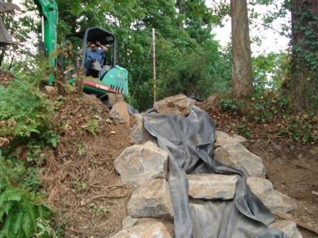 Image of a large piece of equipment at the top of a hill, prepping the landscape for a new water feature design.