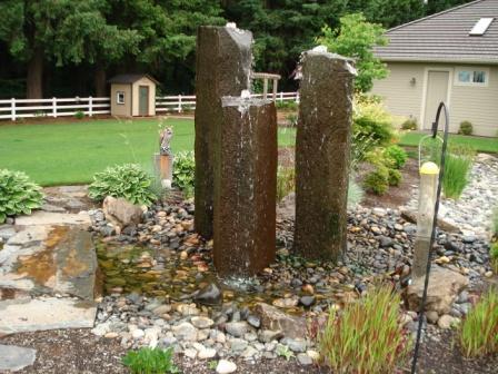 Image of three tall stones with water cascading to a rock garden below, a water feature design by Frontier Landscaping.