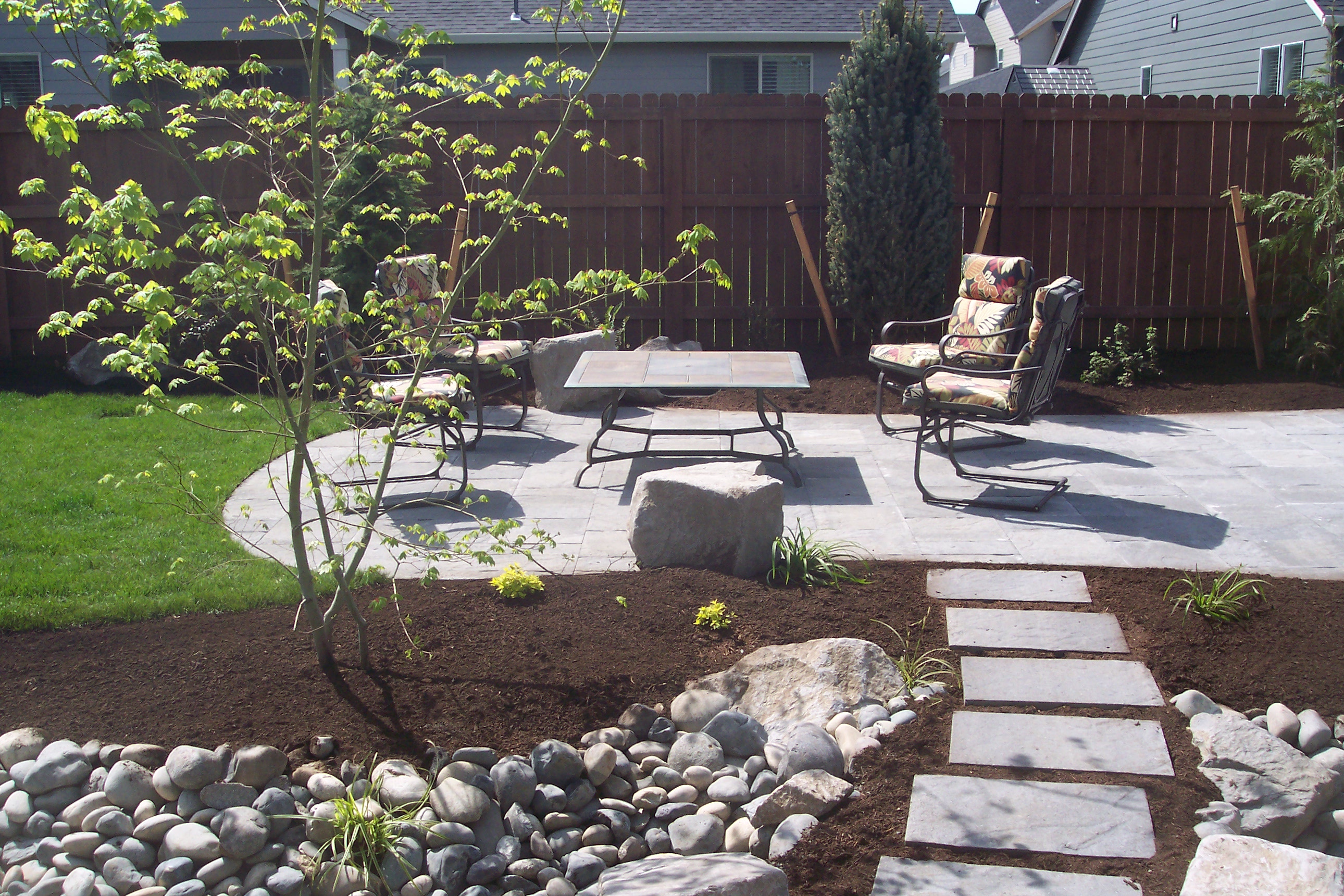 Image of a path and patio with a rock garden along the path, leading to a picnic table on the patio.