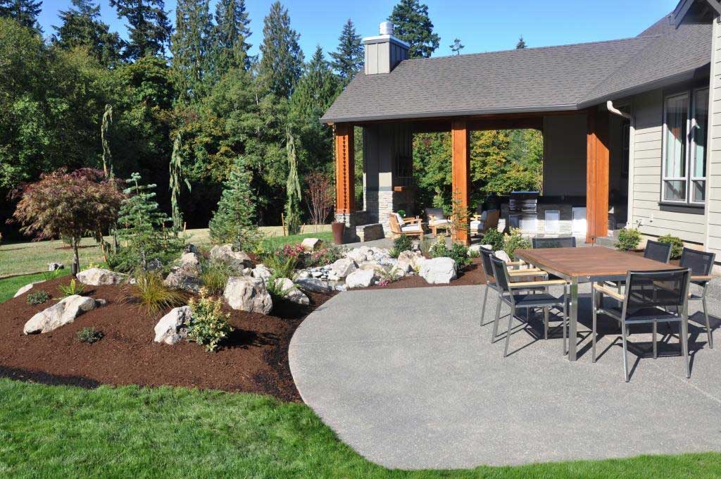 Image of a backyard patio with a picnic table and a landscaped rock garden to its right.