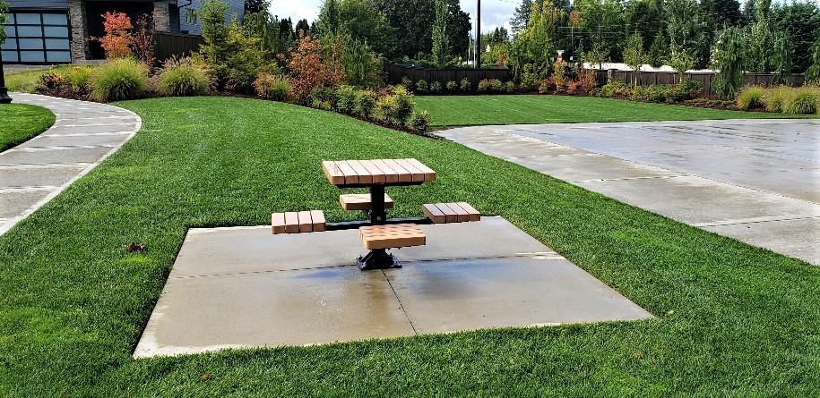 Image of a picnic table and concrete slab surrounded by a well-maintained lawn as part of landscape maintenance services.