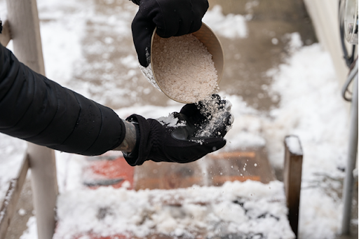 Image of a person's left arm with their right hand pouring de-icing material from a bucket into their left hand.