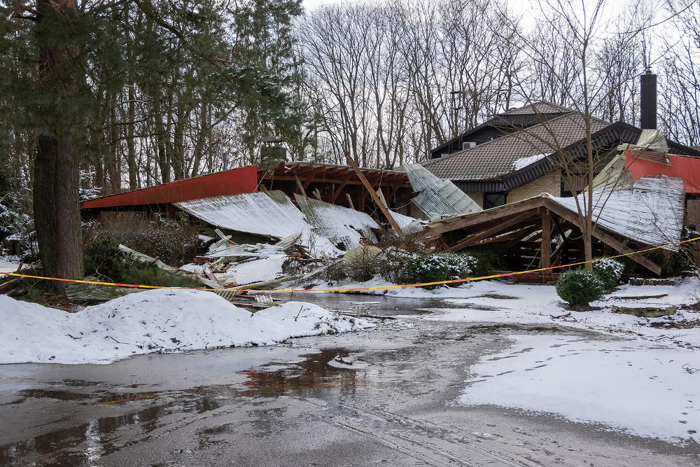 Image of a collapsed home surrounded by snow, damaged from a winter storm.